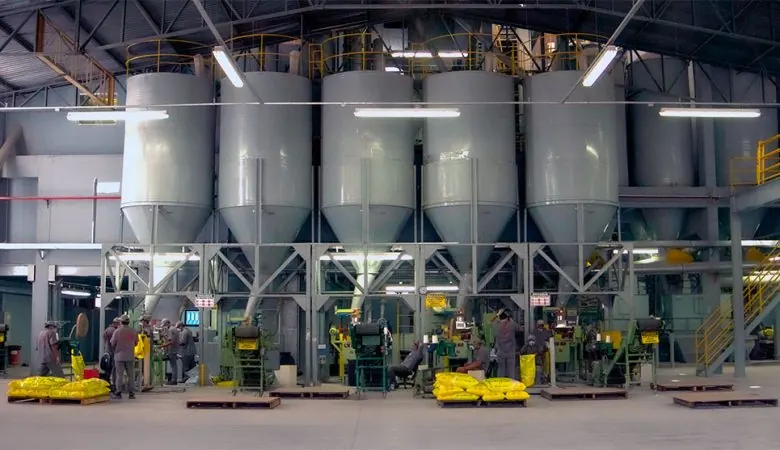 Linha de ensaque de uma fábrica de ração com silos e operadores.