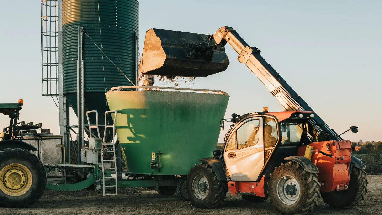 Pá carregadeira abastecendo o vagão forrageiro ao lado do silo.